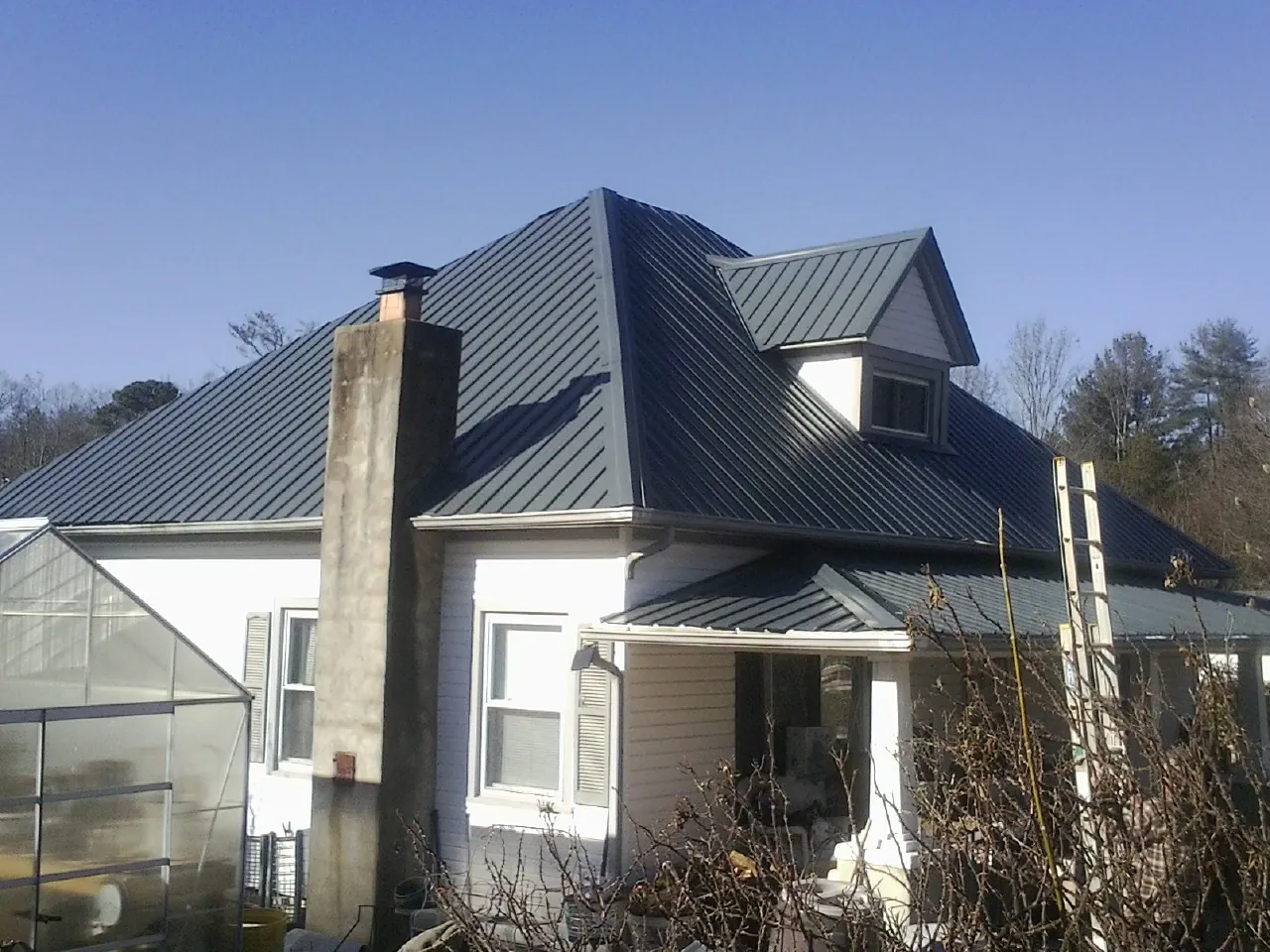 Dark blue standing seam metal roof on a white farmhouse with dormer — Slate & Tile Roof Repair by Roofing Brothers in Avon Park