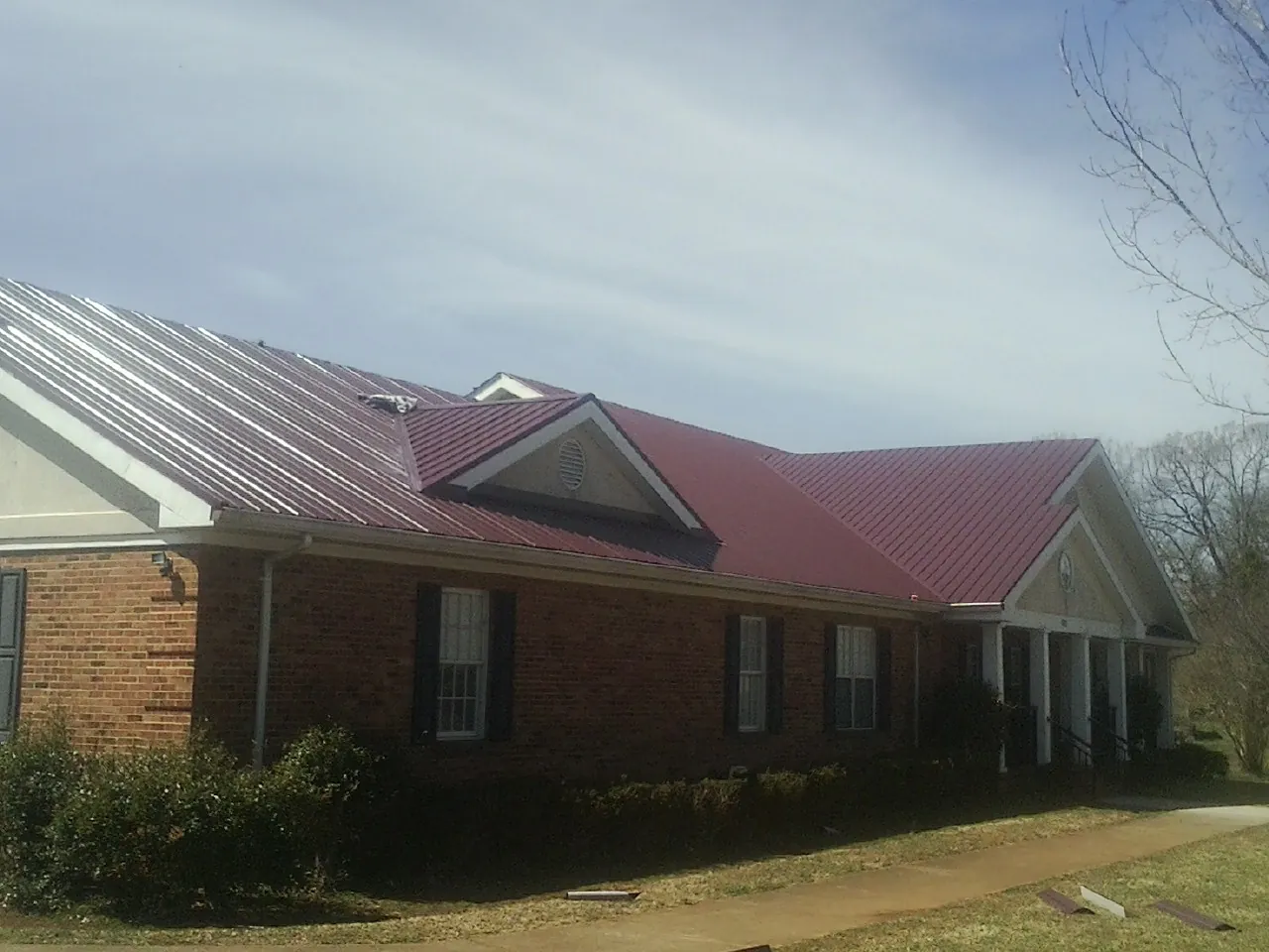 Red metal roof with gabled entries on a long brick building, from a Hail Damage Roof Repair job in Avon Park