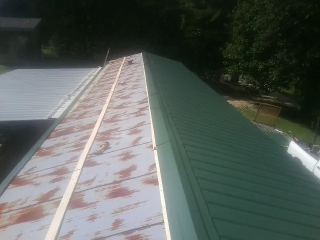 Old rusted panels beside newly installed green metal roofing — Wind Damage Roof Repair by Roofing Brothers in Avon Park