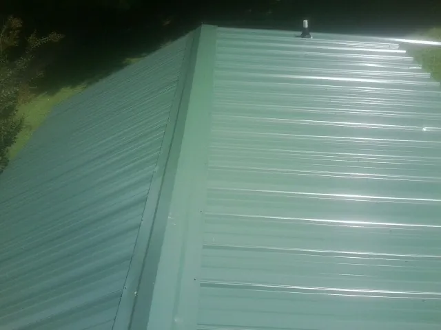 New green metal panels meeting at the ridge of a roof — Flat Roof Repair work by our crew in Avon Park