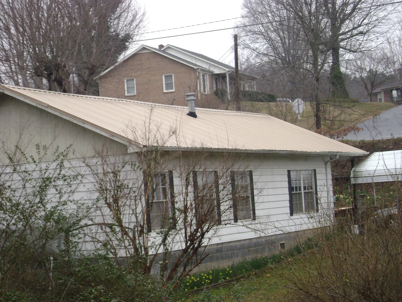 Tan metal roof on a white sided house set into a hillside — Commercial Roofing by Roofing Brothers in Avon Park