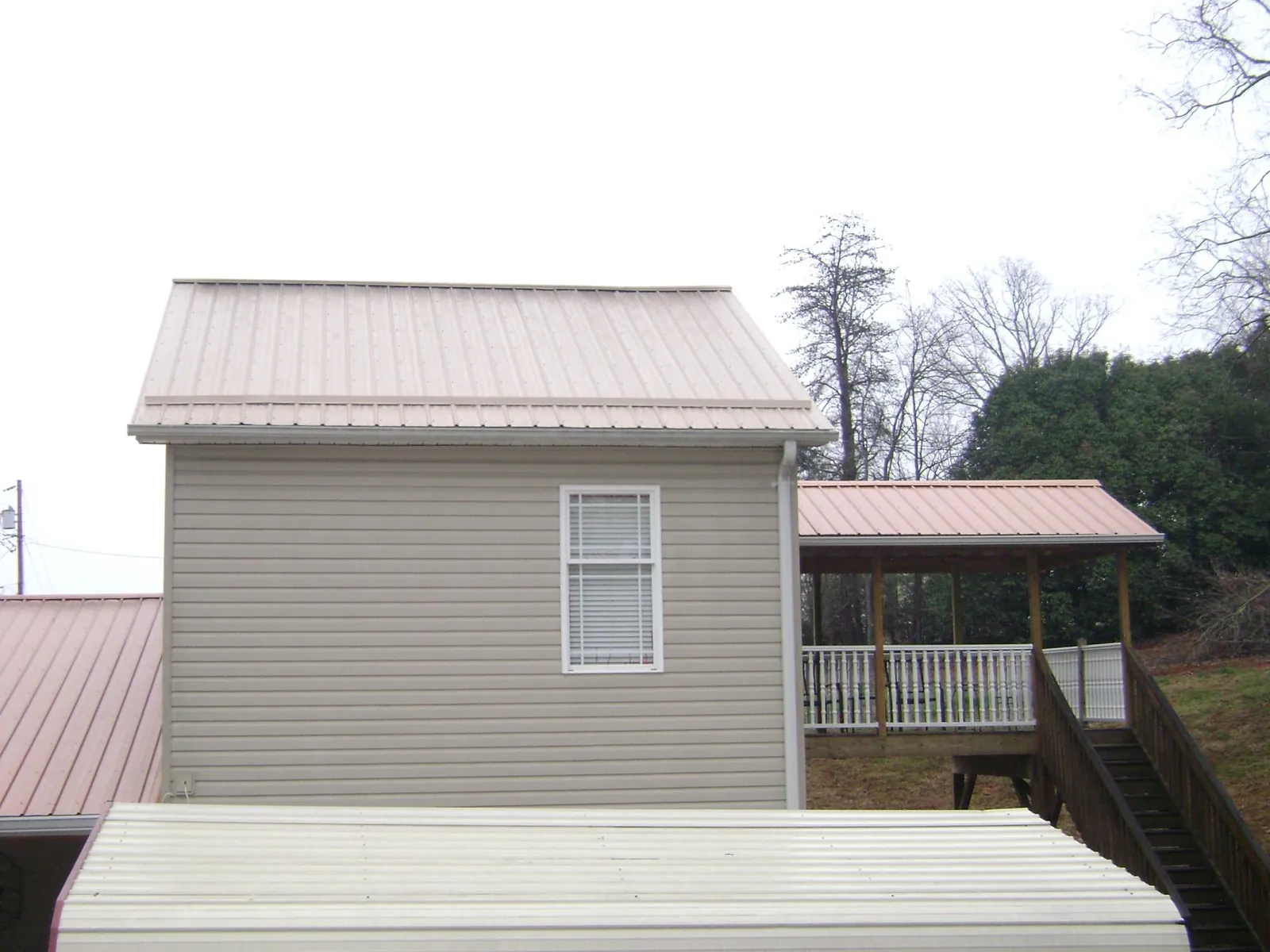 Tan metal roofs on a two story addition and attached porch, from a Roof Replacement job in Avon Park